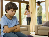 Sedící smutný chlapeček, v pozadí hádající se rodiče.
