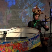 Umělkyně hraje na experimentální hudební nástroj, za ní se odehrává videoprojekce.