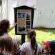 Děti a lektorka si čtou infotabuli u Pardubického zámku.