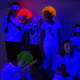 Děti v bílých kostýmech a některé v barených parukách pod UV světlem.