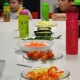 Děti při večeři. Na stole zelenina a barevné plastové lahve. 